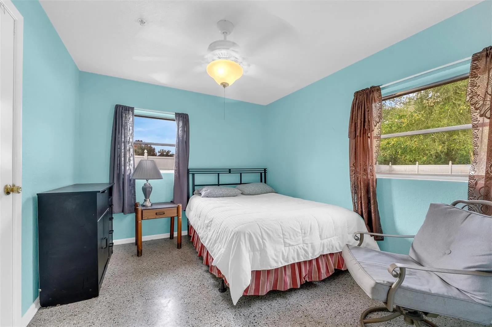 Bedroom with turquoise walls, seating area, dresser, and natural light.