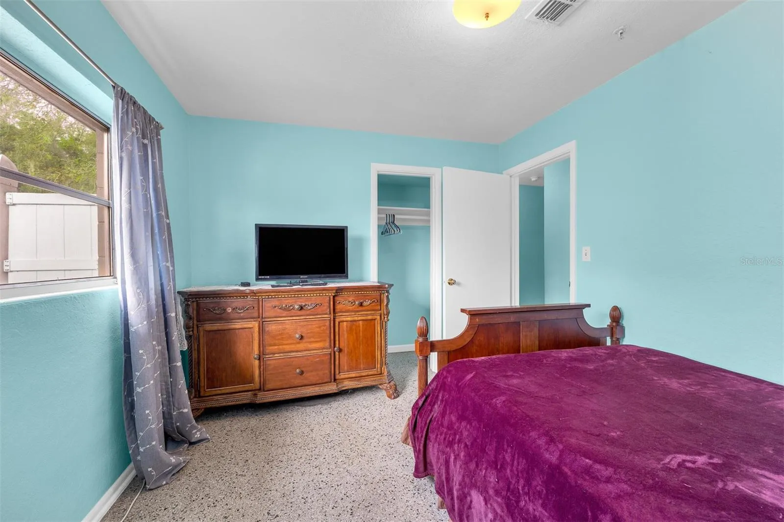 Bedroom angle showing dresser with TV, closet access, and natural light.