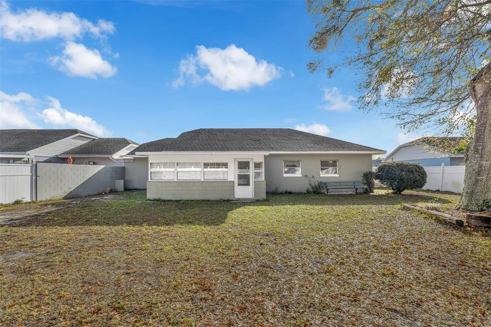 Backyard with enclosed porch, mature tree, and partially fenced yard.