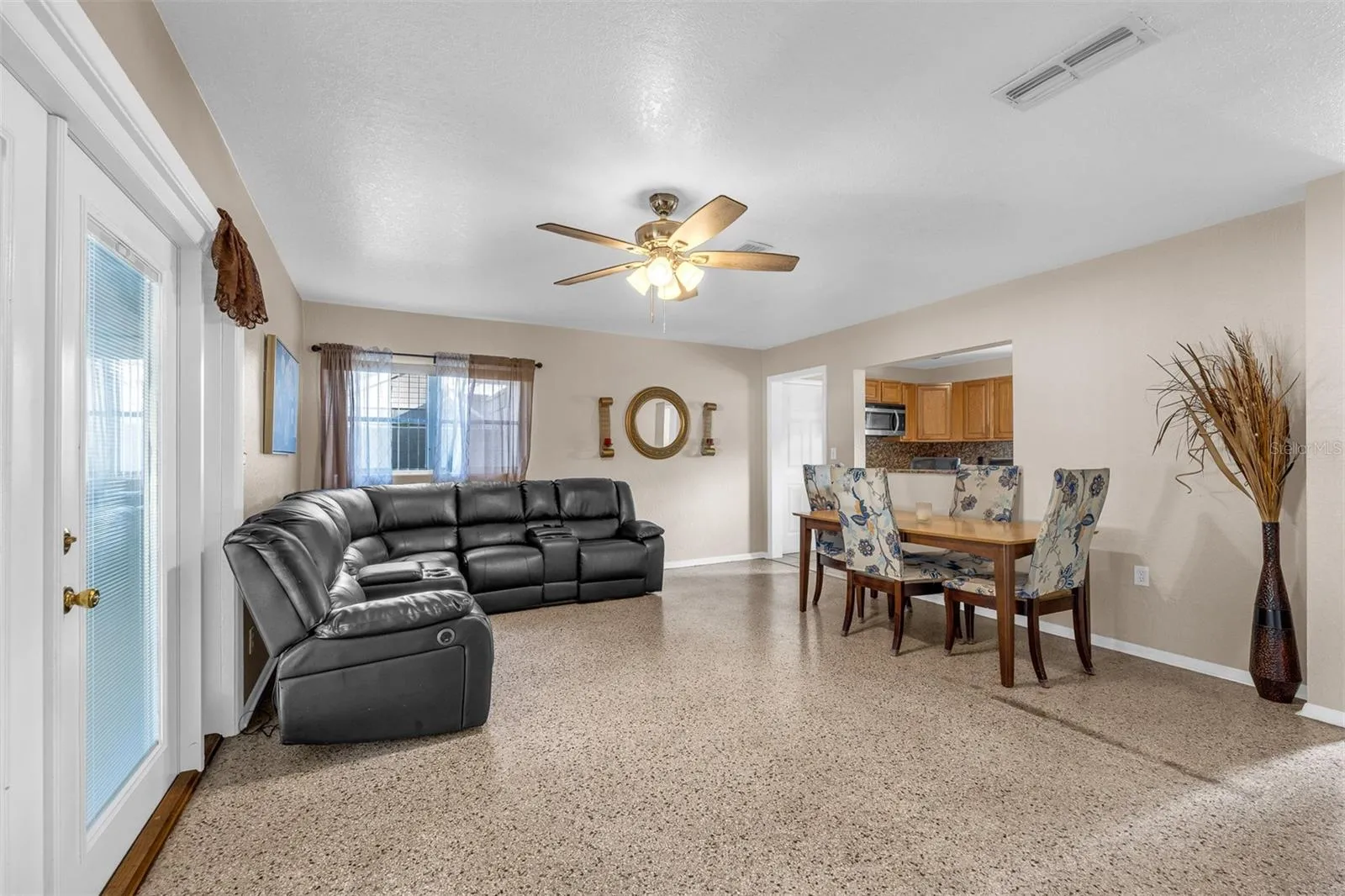 Open layout featuring a dining area with upholstered seating, pass-through window to the kitchen, and polished flooring. Decorative accents and natural light enhance the space.