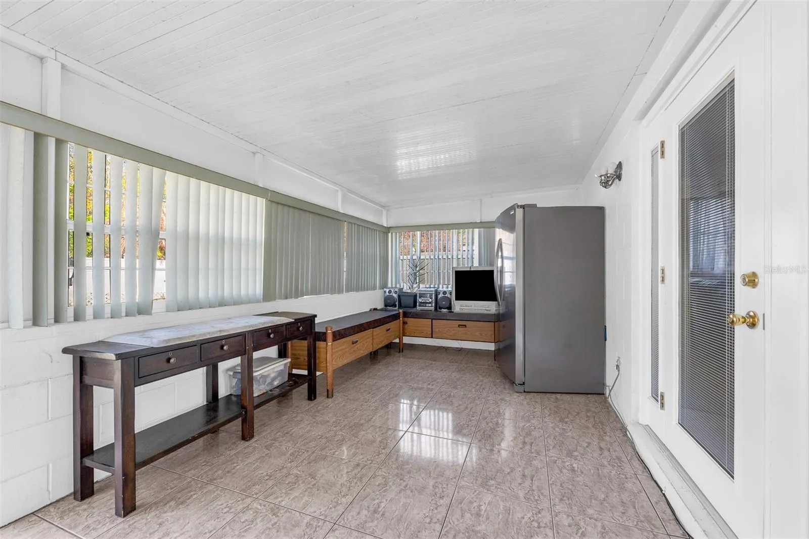 Sunroom with tile flooring, vertical blinds, storage benches, and refrigerator