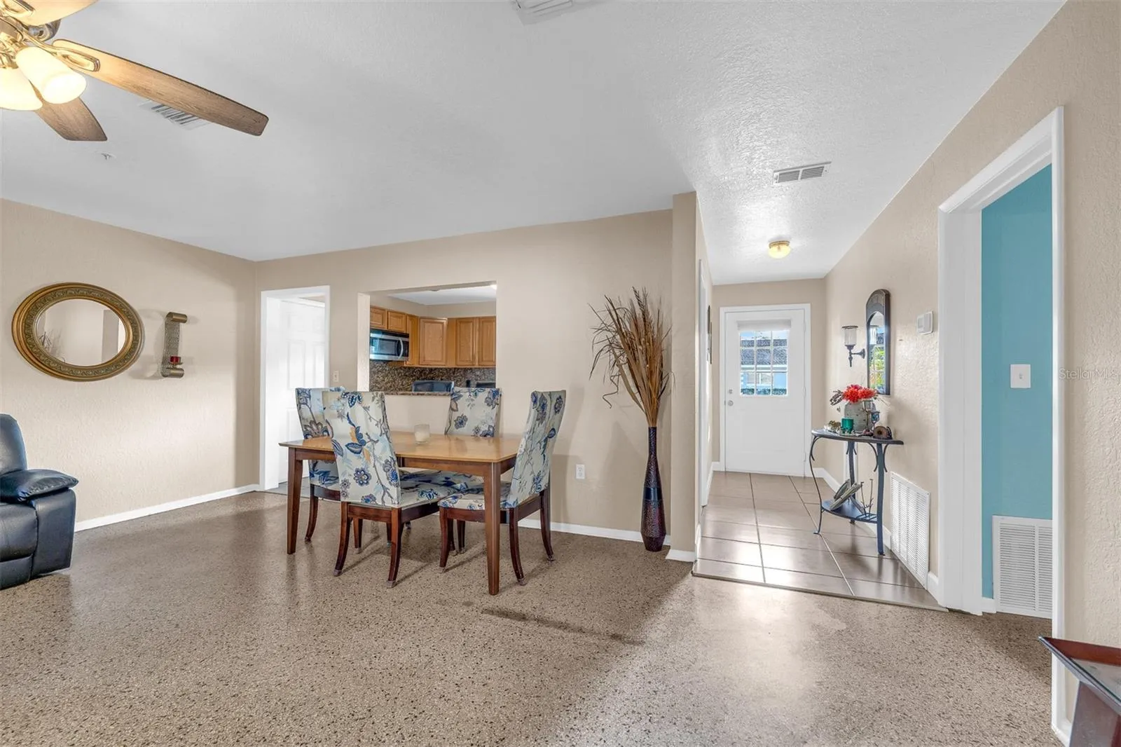 Dining space with a four-seat table, decorative wall mirror, and tall accent vase. Pass-through opening connects directly to the kitchen.