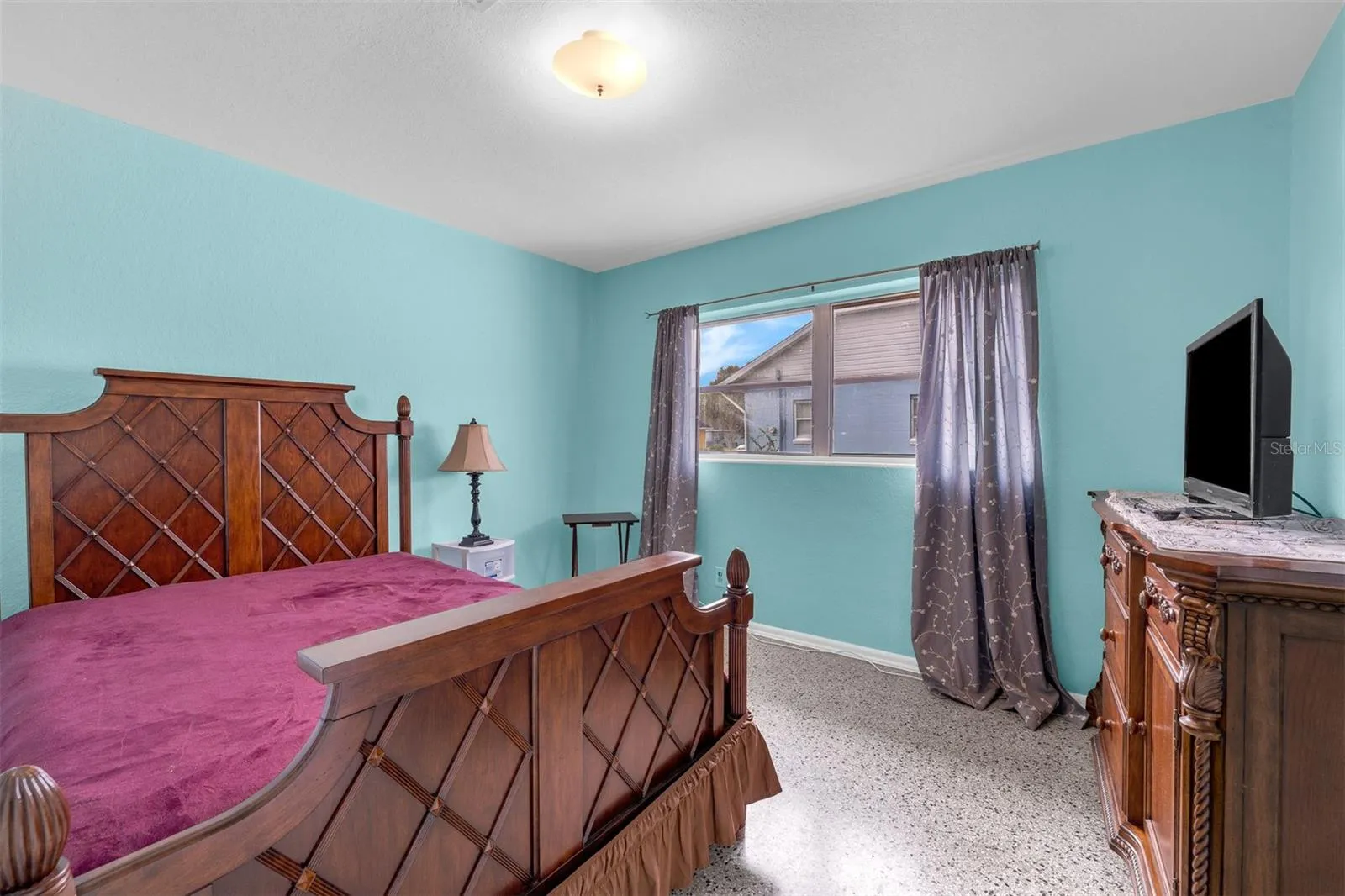 Bedroom with classic wood furniture, maroon bedding, and terrazzo-style flooring.