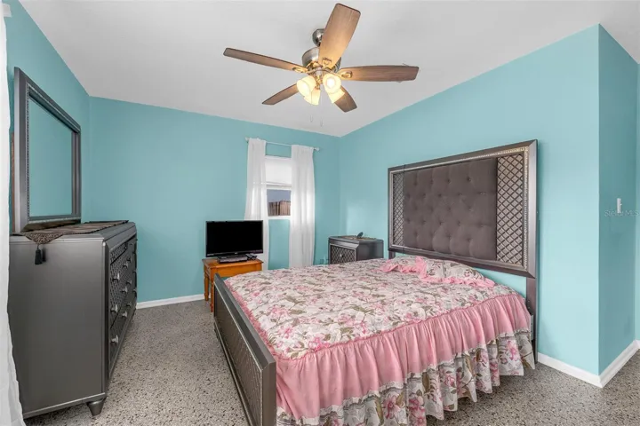 Bright bedroom with multiple windows, dresser with mirror, and coordinated bedding. Terrazzo-style flooring adds durability.