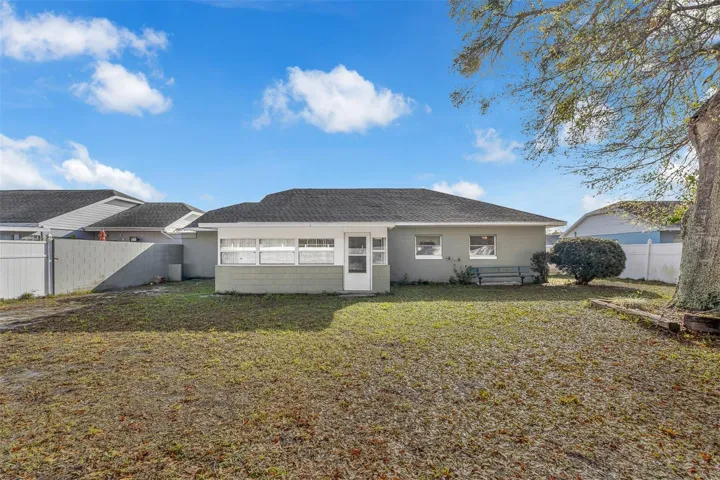 Backyard with enclosed porch, mature tree, and partially fenced yard.