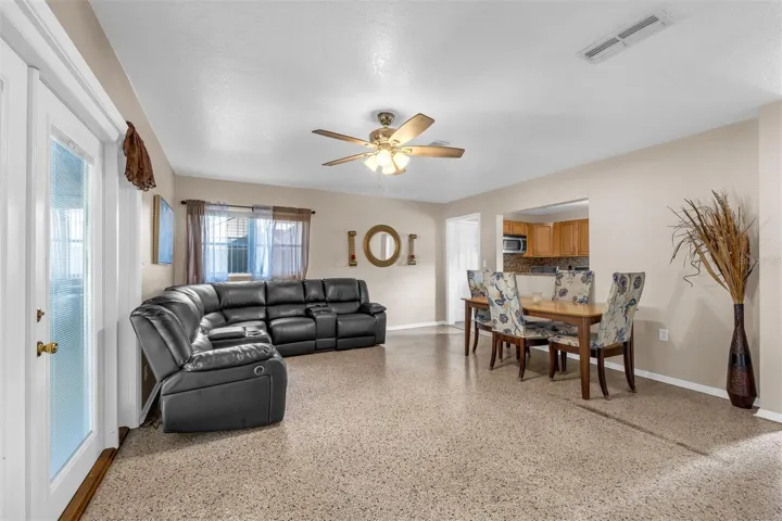 Open layout featuring a dining area with upholstered seating, pass-through window to the kitchen, and polished flooring. Decorative accents and natural light enhance the space.
