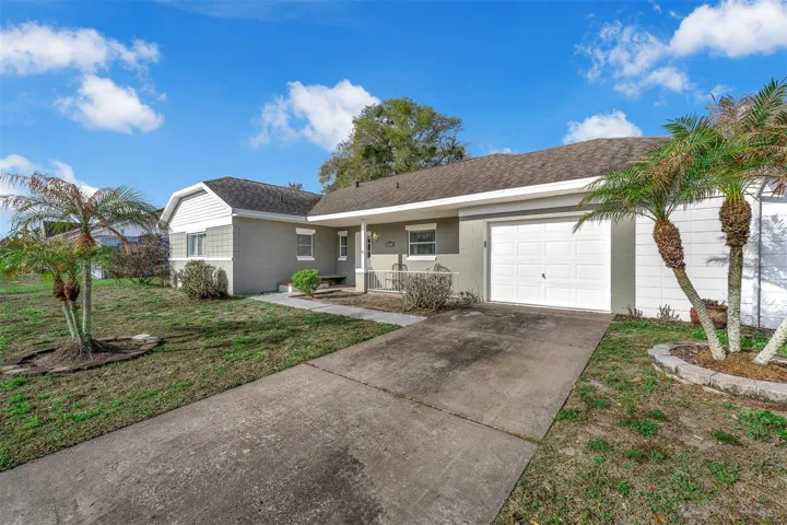 Another view of the home’s exterior showing the driveway, garage, and front porch. Light exterior colors and a simple landscape layout provide easy-maintenance curb appeal.