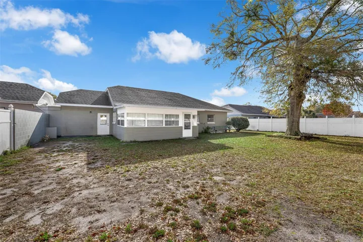 Backyard with vinyl privacy fence, shade tree, and access to sunroom.