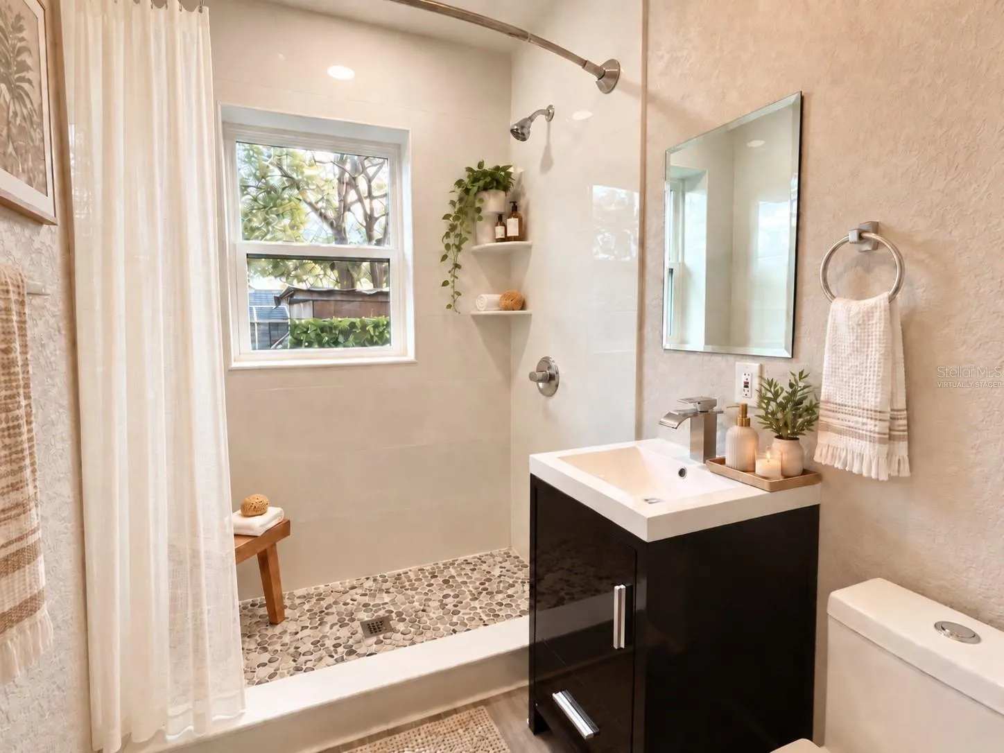 Virtually Staged - Renovated bath with walk-in shower, pebble flooring and modern vanity.