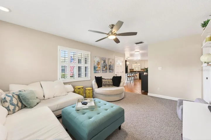 The warm and inviting Living Room features plush luxury carpet, plantation shutters, a stylish ceiling fan, and wall shelving, creating a cozy yet refined space.