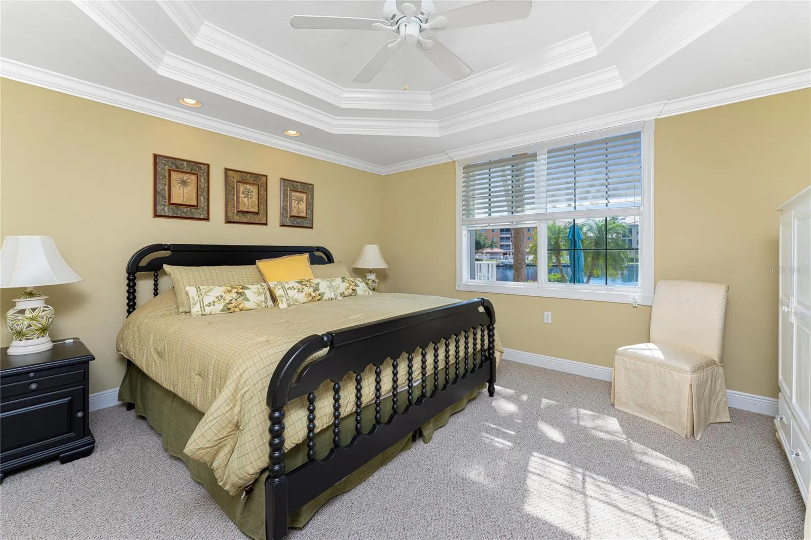 Sun-lit master bedroom beautifully finished with double tray ceiling with crown inlay overlooking a serene water view.