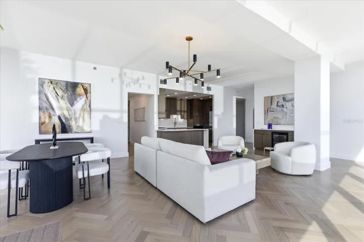 From the vantage, the full breadth of the living space unfolds - herringbone flooring set on axis, with southern light moving across the pattern, connecting dining, seating, and kitchen within a continuous open expanse.