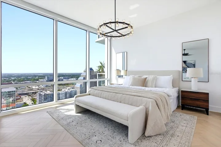 Set at end of the suite, the bedroom framed in expansive city views, with an elegant crystal chandelier on dimmer adding a soft ambient glow.
