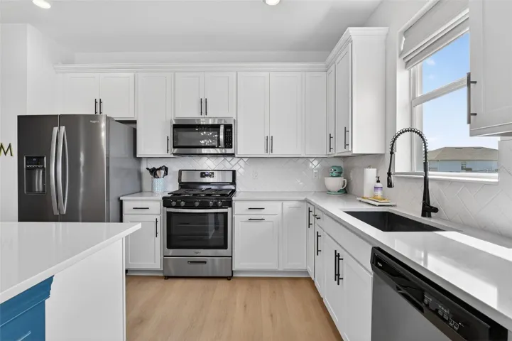 Kitchen featuring stainless steel appliances, white cabinetry backsplash, and recessed lighting