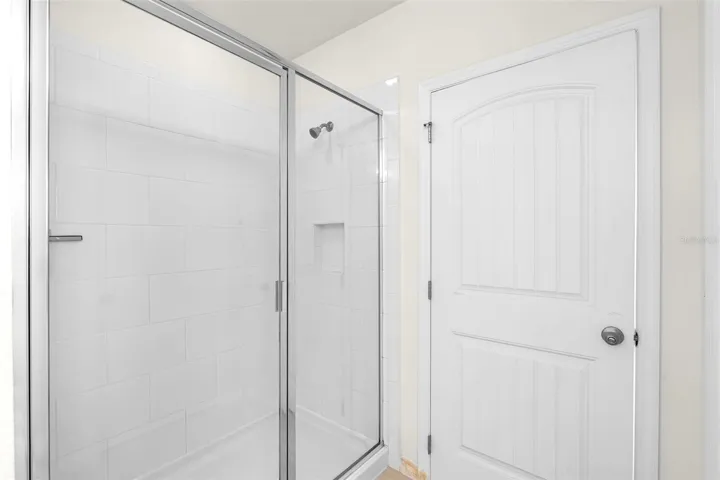 Shower with Upgraded Rectangular Tile, Glass Doors and Shampoo Niche.