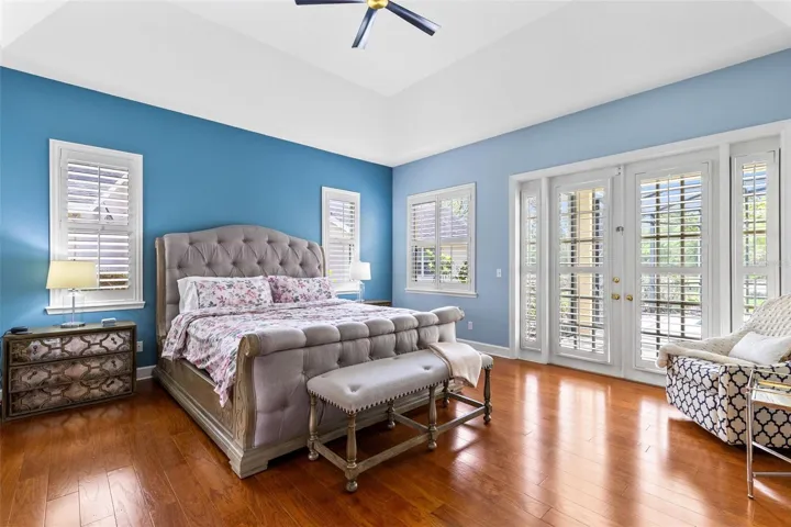 THE LARGE PRIMARY BEDROOM FEATURES LOTS OF WINDOWS, SLIDING DOORS OUT TO THE POOL AND PLANTATION SHUTTERS WITH WOOD FLOORING.