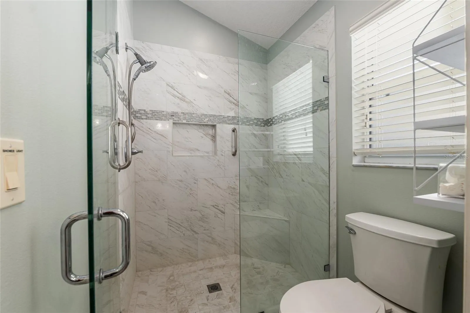 Primary Shower: Walk-in shower with tile surround, glass enclosure, and built-in niche offers a clean, modern design.