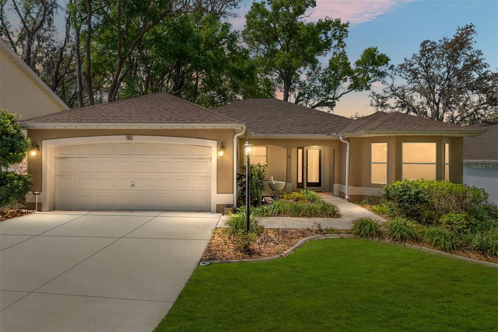 Front Exterior (Twilight): Evening view highlights exterior lighting and a warm, inviting entrance framed by lush greenery.