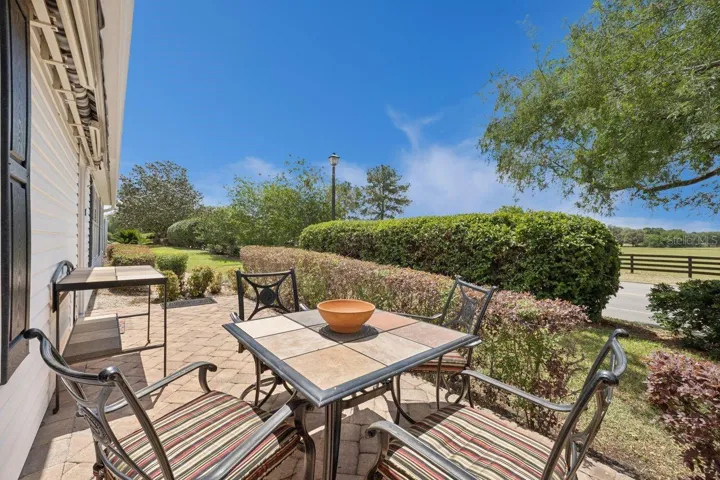 Patio area with Outdoor table, 4 chairs with cushions & serving high-top table. Awning is closed. View over to Tortoise Preserve.