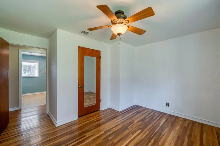 Bedroom with wood floors, a ceiling fan, and direct access near the bath area. The simple layout offers flexibility for guests, office space, or everyday living.