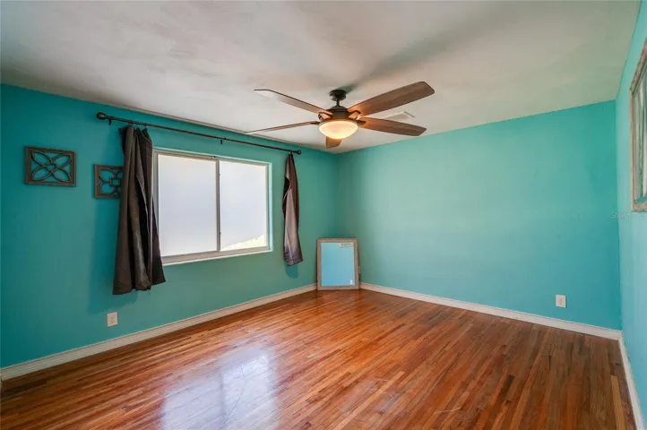 Bright primary bedroom with wood floors, a ceiling fan, and a large window that brings in natural light.