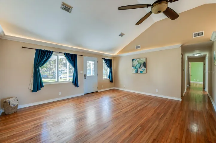 Sunlit living room featuring wood floors, crown molding, and front-facing windows for abundant natural light. A vaulted ceiling and open sightlines make the space feel expansive.