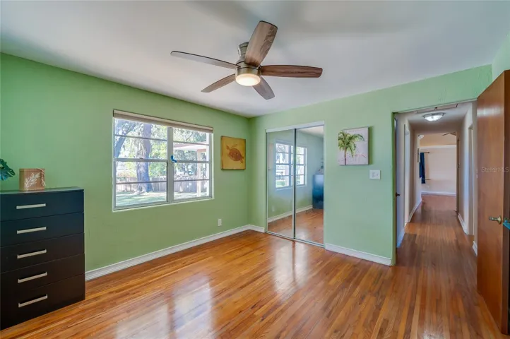 Bedroom with wood floors, mirrored closet doors, and a functional layout with easy access to the main hallway. A large window enhances the bright, airy atmosphere.