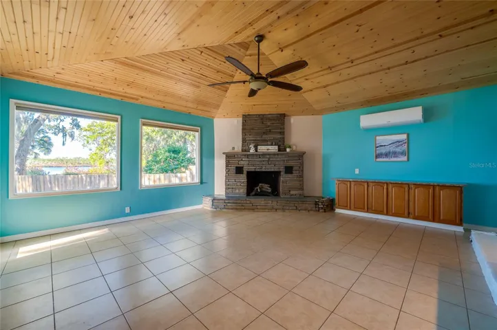 Spacious family room featuring a vaulted wood ceiling, stone fireplace, and generous windows that bring in natural light and showcase the waterfront setting. Built-in cabinetry adds convenient storage.