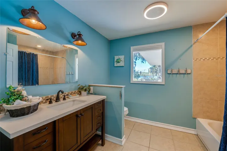 Updated bathroom with a modern vanity, solid-surface countertop, and tiled tub surround. A window brings in natural light and adds to the bright, refreshed feel.