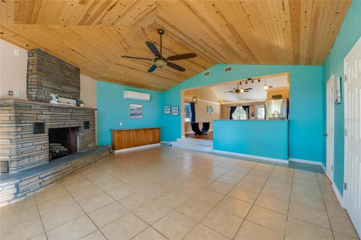 Open family room with tile floors, a wood ceiling, and a prominent stone fireplace. The connection to the main living and kitchen areas supports easy everyday flow.