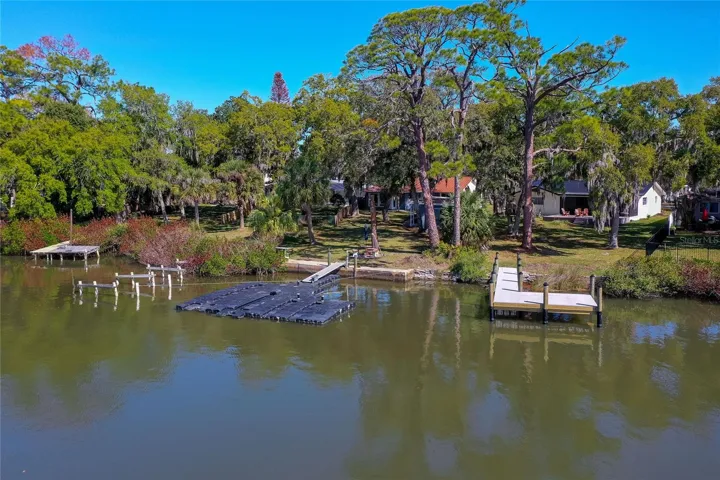 Aerial waterfront view showcasing the property’s shoreline, expansive backyard, and private dock from across the water. The setting highlights the home’s peaceful waterfront presence.