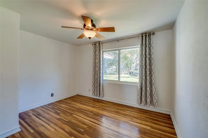Bedroom with wood floors, a ceiling fan, and a large window overlooking the front yard. A simple, comfortable space ready for a variety of uses.
