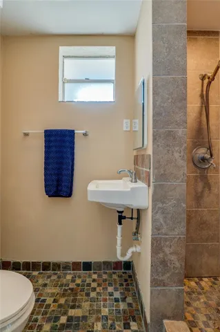 Bathroom featuring a tiled walk-in shower, mosaic tile flooring, and natural light from the window. A practical layout designed for convenience.