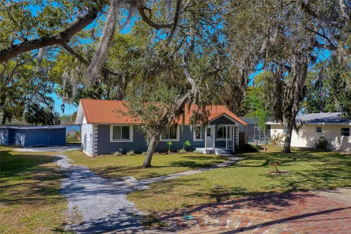 Front and side exterior view highlighting the home’s updated exterior, broad yard, and water glimpses beyond. Mature oaks add character and shade to the property.