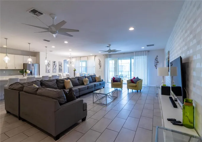 Expansive living area flooded with natural light from large windows overlooking the covered lanai, private pool, and spa. The space features a large smart Tv. Elegant wall decor adds a touch of sofistication.