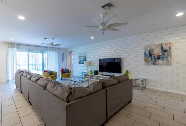 Expansive living area flooded with natural light from large windows overlooking the covered lanai, private pool, and spa. The space features a large smart Tv. Elegant wall decor adds a touch of sofistication.