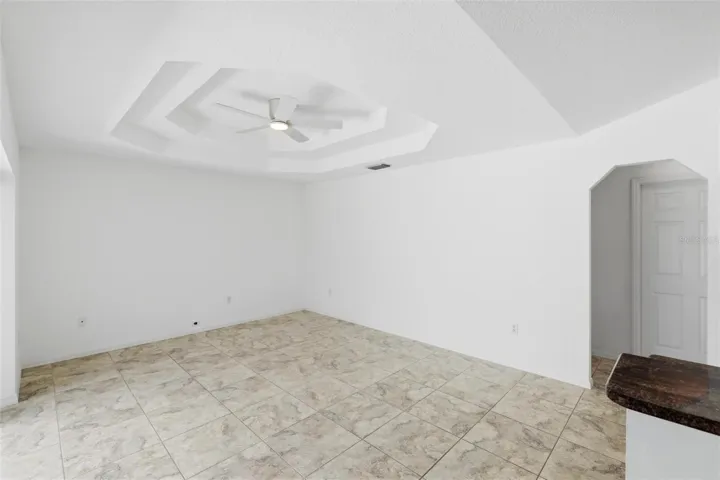 Open living and sitting area adjacent to kitchen with neutral tile floors and abundant natural light