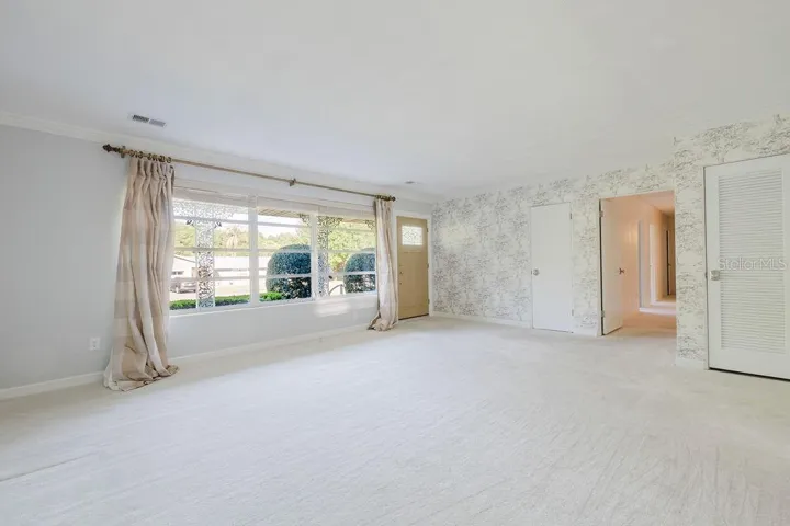 Living room with view of over sized windows and front door. Coat closet for storage.