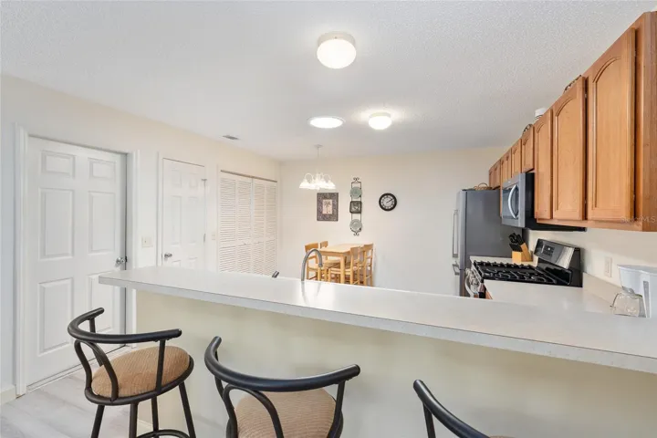 KITCHEN view - Shows BREAKFAST BAR with bar stool seating (front Center), GAS STOVE (R), SOLAR TUBE (Center in ceiling), INDOOR LAUNDRY behind louvered bi-fold doors (back Center), CLOSET PANTRY (2nd door from L) and access door to 1.5 Car Garage (far L)