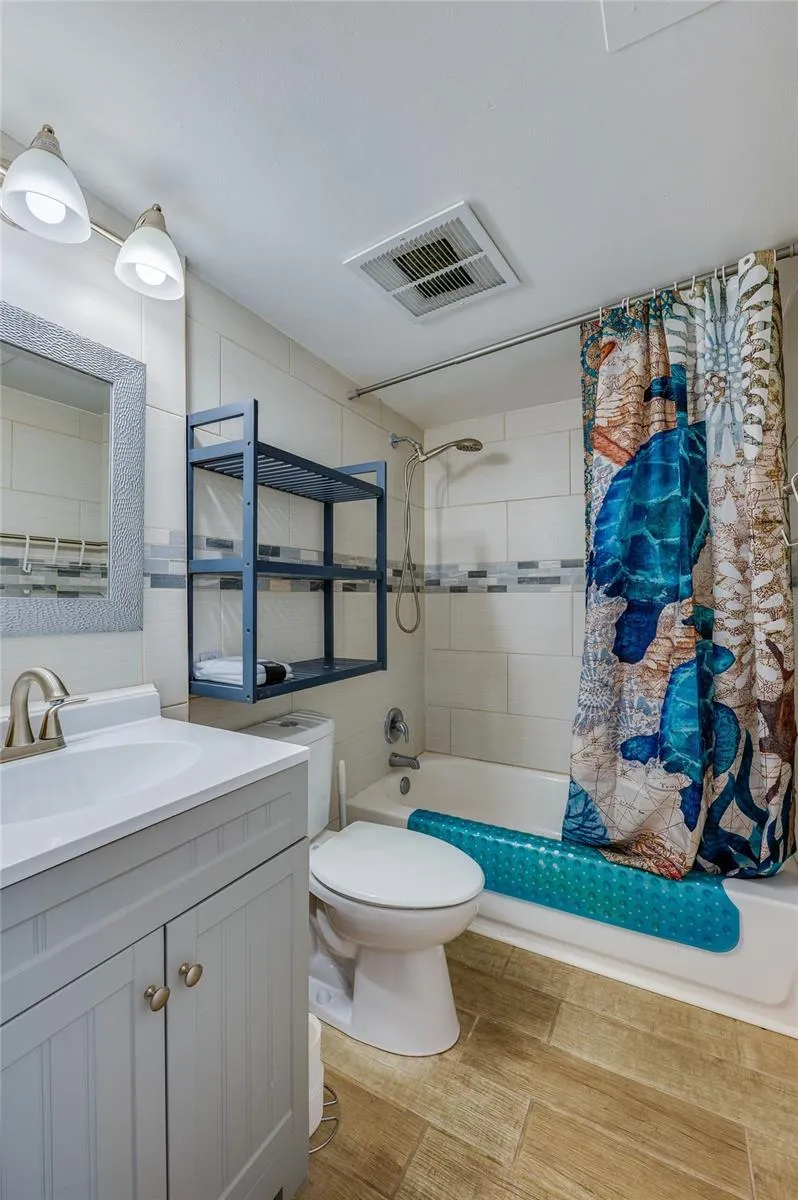 Full bathroom featuring a modern-style vanity, tiled tub/shower surround, and added shelving for practical everyday storage.