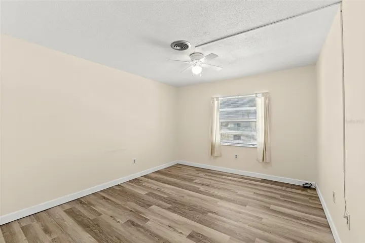 Primary bedroom with wood-look LVP flooring, ceiling fan, and window — Ocean Park South unit G20