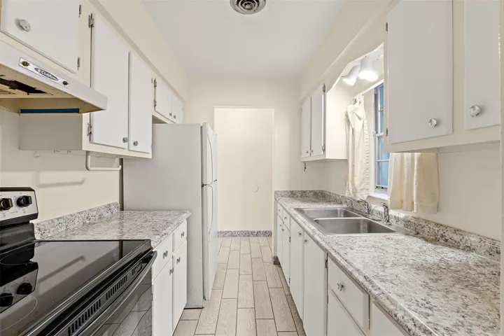 Galley kitchen with white cabinets, granite-look countertops, double sink, and new electric range
