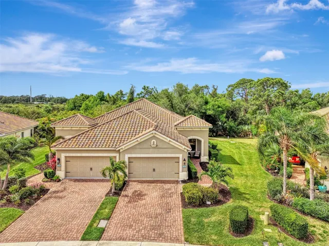 Villa on the right side with paver driveway and tile roof.