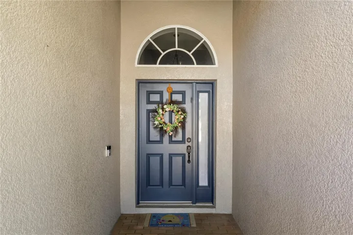 Charming front entry featuring a navy blue double door with sidelight and transom window, accented by a welcoming floral wreath and covered brick porch.