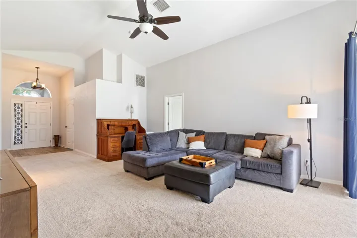 Spacious living room featuring high ceilings with a modern ceiling fan, built-in architectural details, and abundant natural light from the arched entryway.