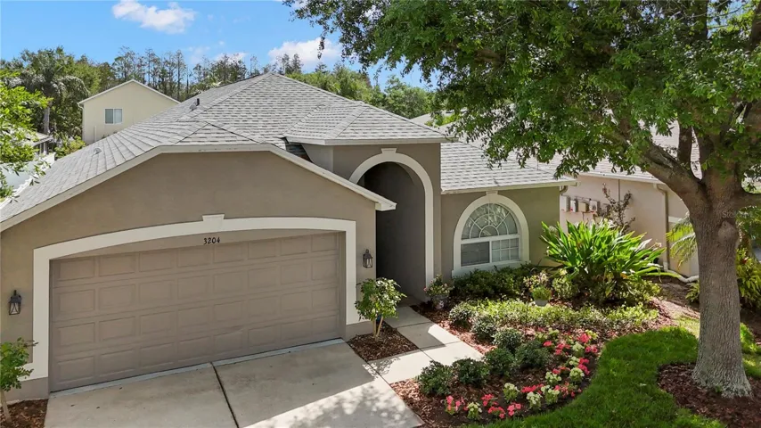 This home boasts a clean neutral façade, arched entry, and vibrant curb appeal with lush landscaping and a mature shade tree.