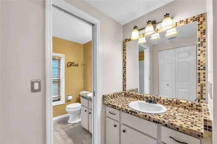 Second vanity and storage closet separated with a pocket door outside of full bathroom with tub/shower combination.