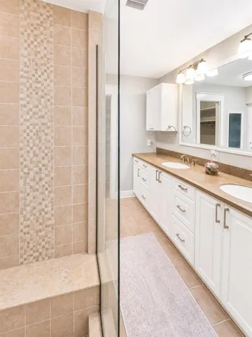 Private primary bath with a spacious tiled shower, custom built-in bench, long dual vanity, and a clean spa-like feel.