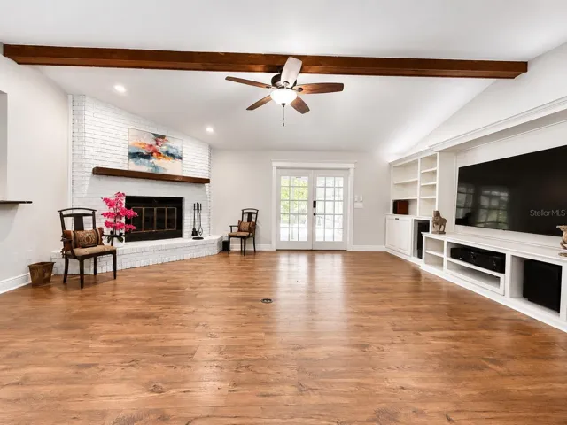 A warm and elegant living space designed to impress, featuring soaring ceilings, rich luxury flooring, exposed beam, a charming white brick fireplace, an beautiful natural light. This room offers the perfect blend of comfort, character, and elevated style.