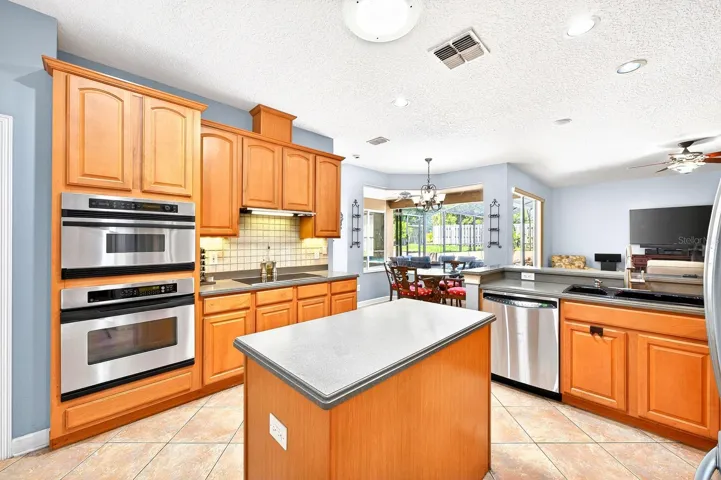 The open concept kitchen is the heart of the home, offering 42” cabinetry, STAINLESS STEEL APPLIANCES, pantry storage, a prep ISLAND, and breakfast bar seating – all overlooking a light-filled breakfast nook and your private SCREENED POOL.